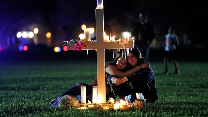 FILE - People comfort each other as they sit and mourn at one of seventeen crosses, Feb. 15,...