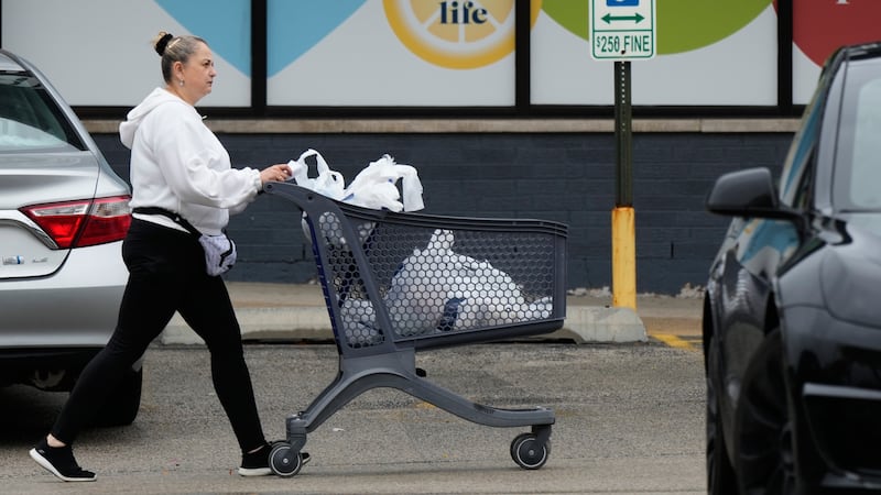 A woman pushes a shopping cart as she leaves a grocery store in Arlington Heights, Ill.,...