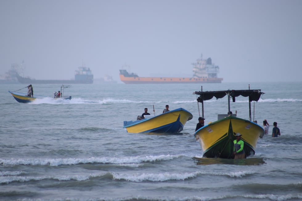 Small boats line the shore as cargo ships and other commercial vessels appear anchored in the...